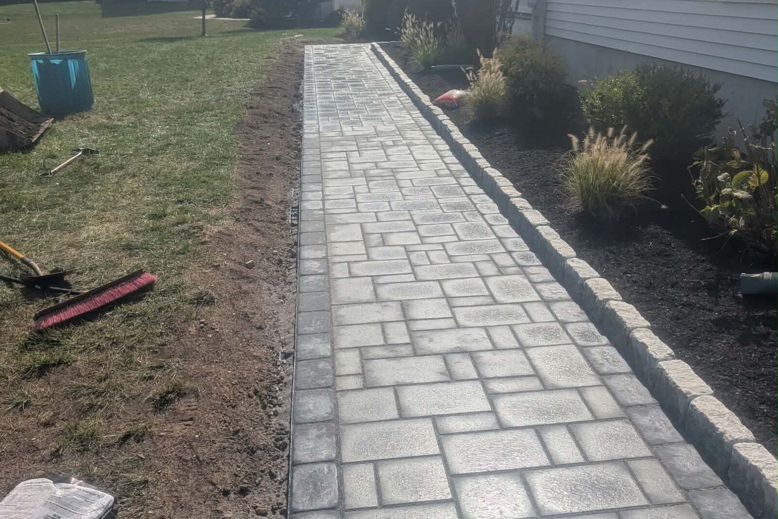 A straight stone walkway with a raised edge course beside a planting bed.